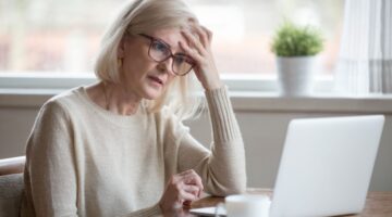 A retired woman looking worried while using a laptop.