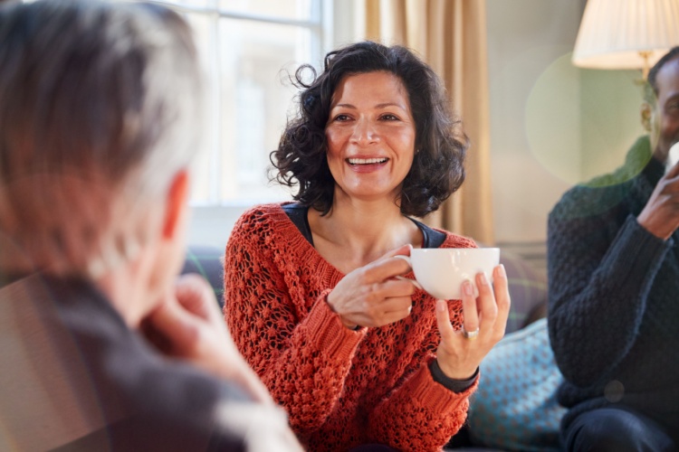 A woman talking to a man while drinking tea.